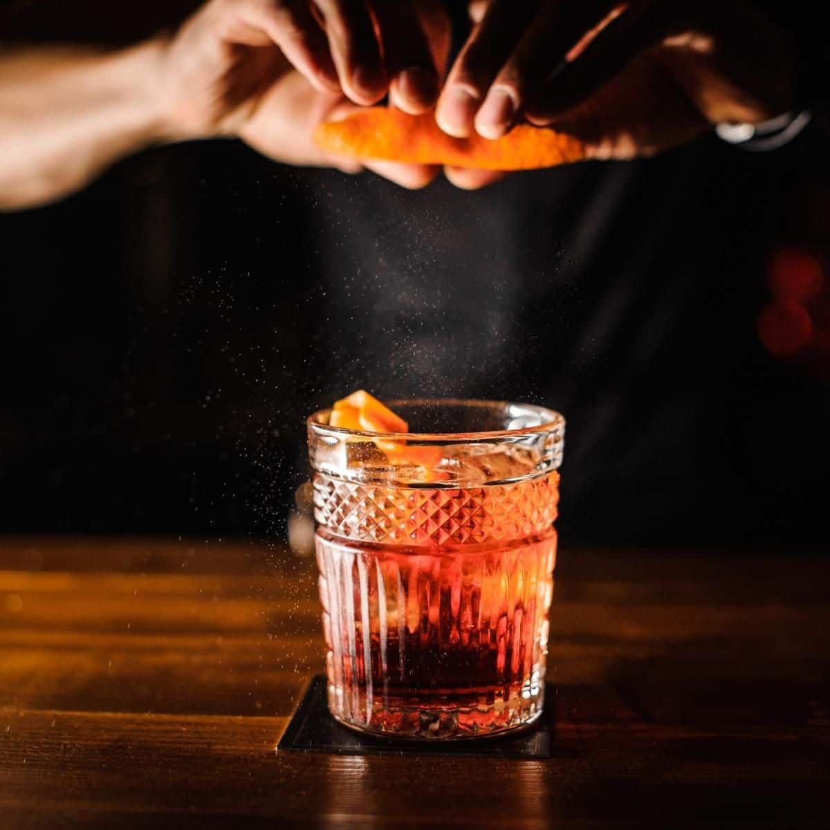 cut crystal glass on table, with hands squeezing an orange peel