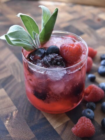 three quarts view of a glass with ice mixed berries and sage garnish with berries on the side