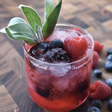overhead view of a glass with ice mixed berries and sage garnish with berries on the side