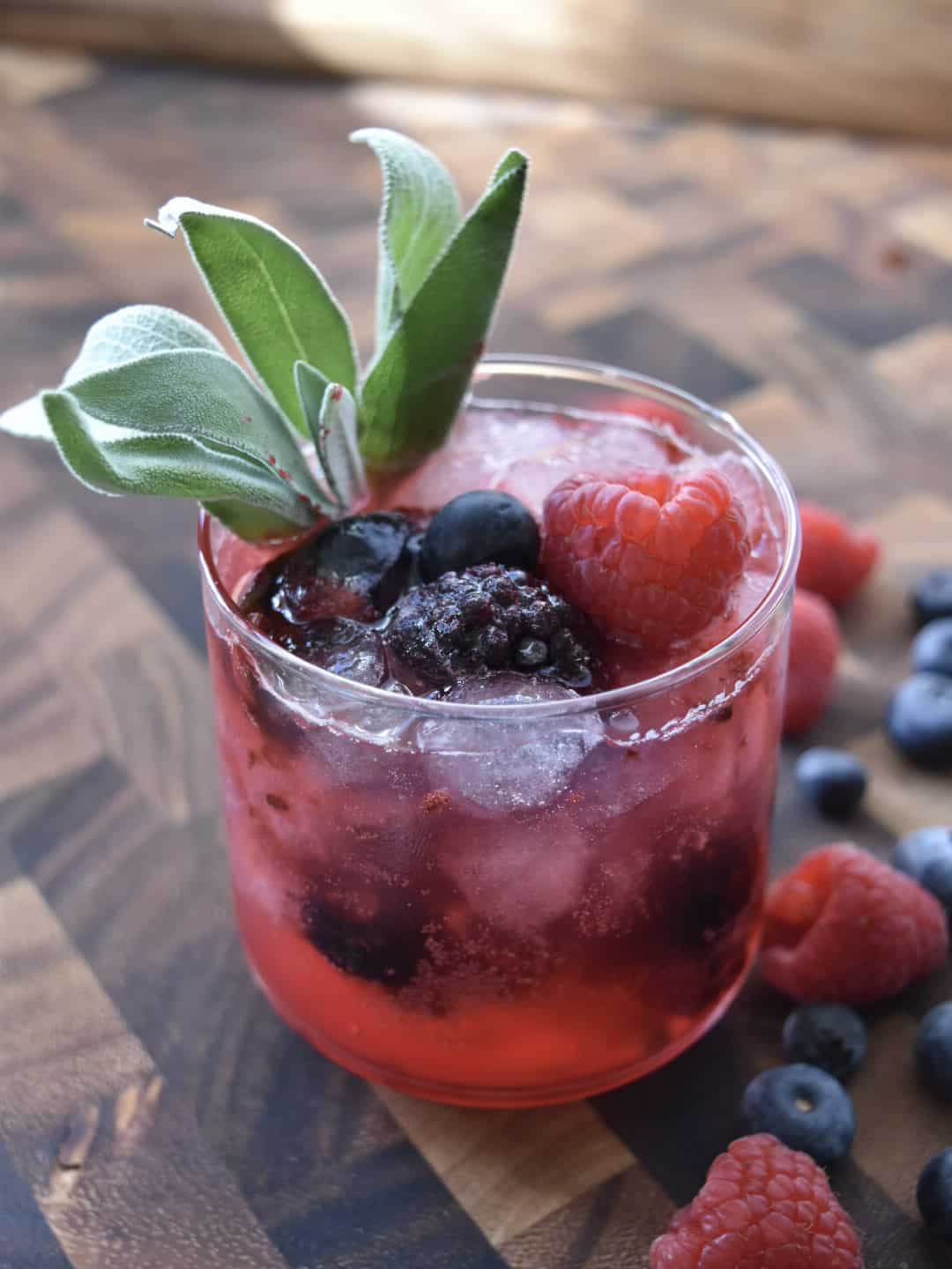overhead view of a glass with ice, mixed berries, and sage garnish with berries on the side.