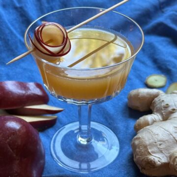 Apple cider and ginger mocktail with apple garnish on a blue cloth.
