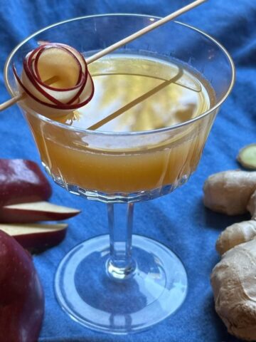 Apple cider and ginger mocktail with apple garnish on a blue cloth.