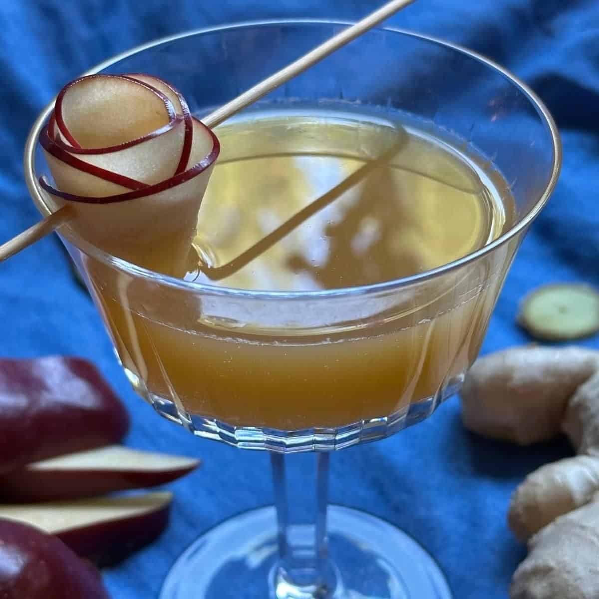 Apple cider and ginger mocktail with apple garnish on a blue cloth.