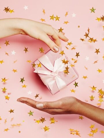 One woman's hand passing a gift to another woman's hand.