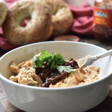 Chipotle in adobo sauce schmear in a bowl on a cutting board with bagels in the background.