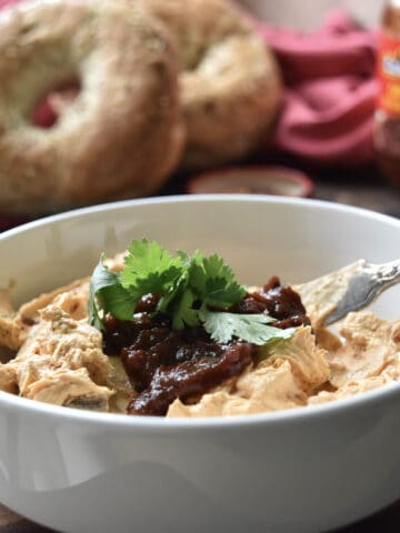 Chipotle in adobo sauce schmear in a bowl on a cutting board with bagels in the background.