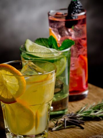 Orange, lime, and berry drinks on a cutting board.