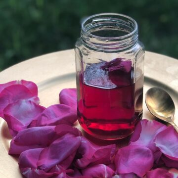 Rose syrup in a glass jar, on a gold plate with rose petals.