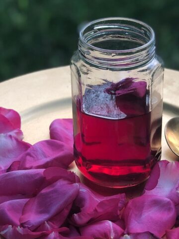 Rose syrup in a glass jar, on a gold plate with rose petals.