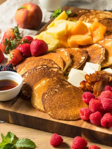 Pancakes, fruit, bacon, and berries on a wood board.