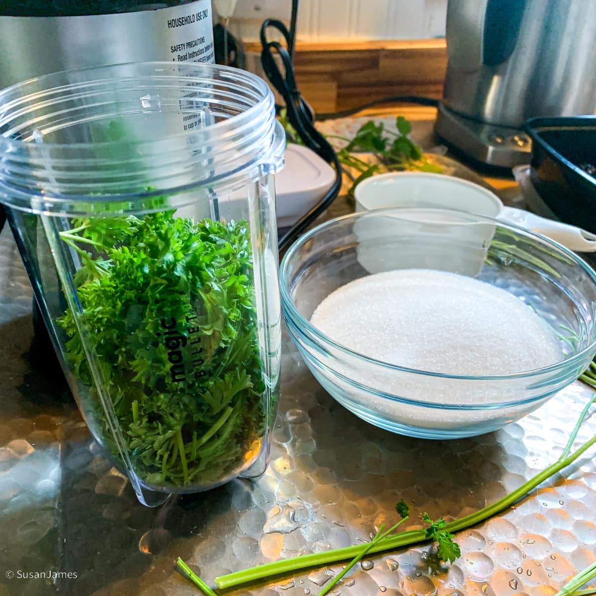 sugar, parsley in a blender cup, and water on a tray.
