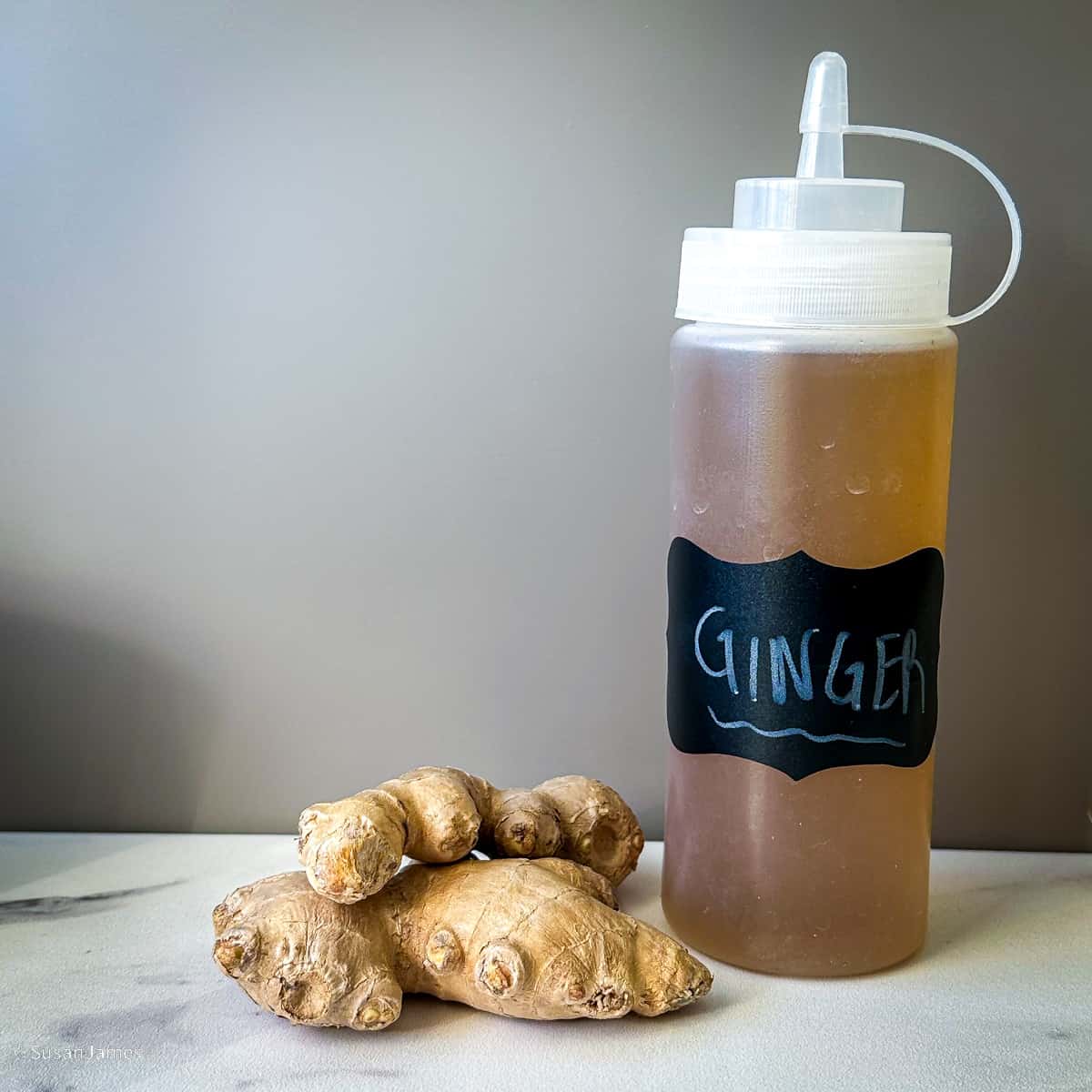 fresh ginger and ginger syrup in a bottle on a table