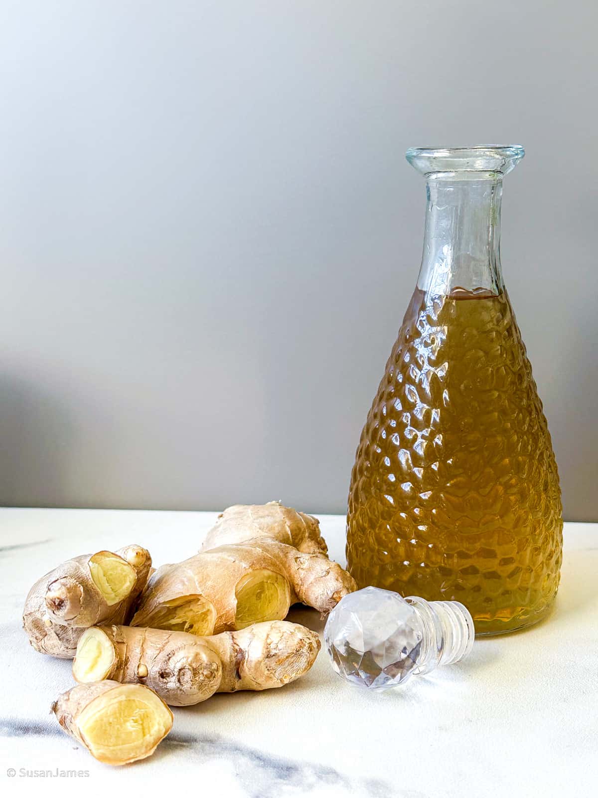 fresh ginger and ginger syrup in a bottle on a table