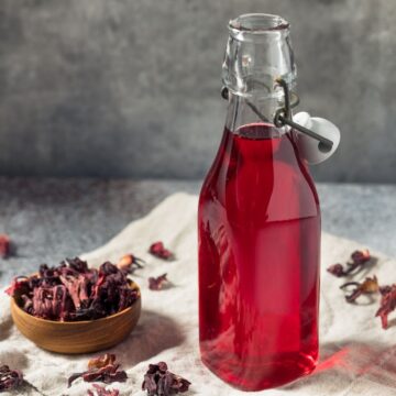 A bottle of Hibiscus Simple Syrup on a napkin with dried hibiscus flowers on the side.
