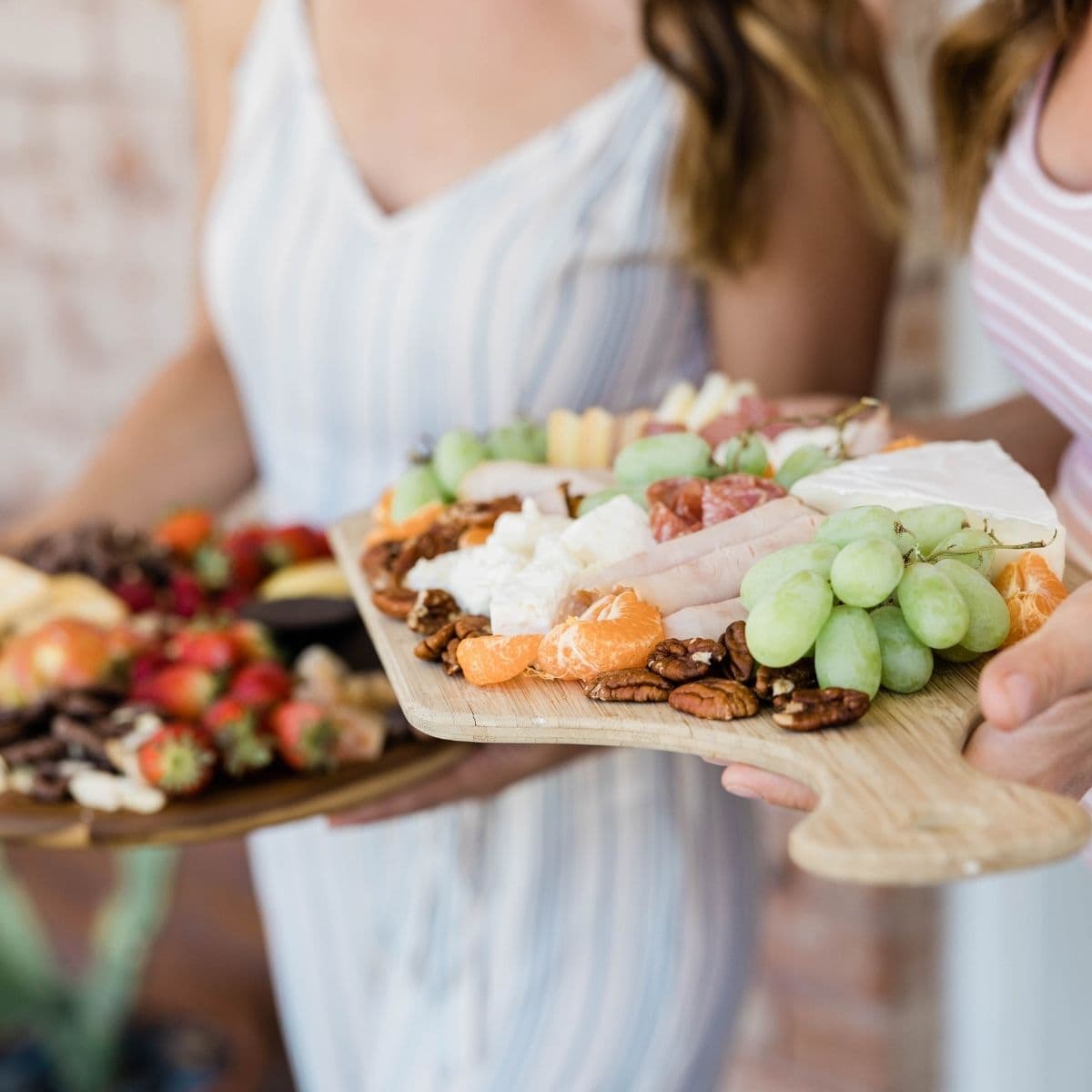 Two women holding small charcuterie boards.