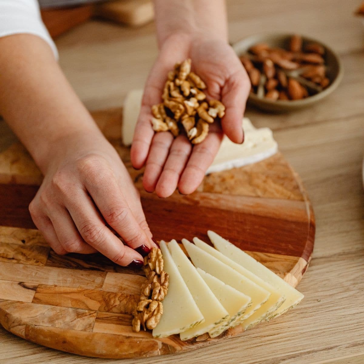 A woman arranging walnuts and cheese on a round cutting board.