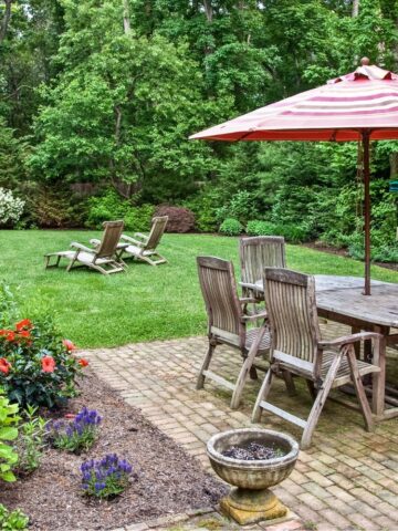 Wood picnic table on a brick patio with six chairs and an umbrella.