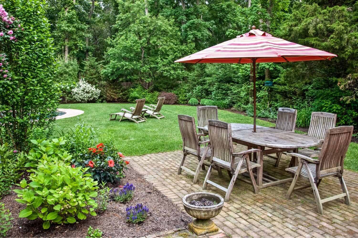 Wood picnic table on a brick patio with six chairs and an umbrella.