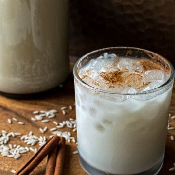 Horchata in a glass on a wood board with cinnamon sticks and rice.