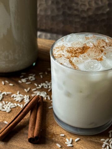 Horchata in a glass on a wood board with cinnamon sticks and rice.
