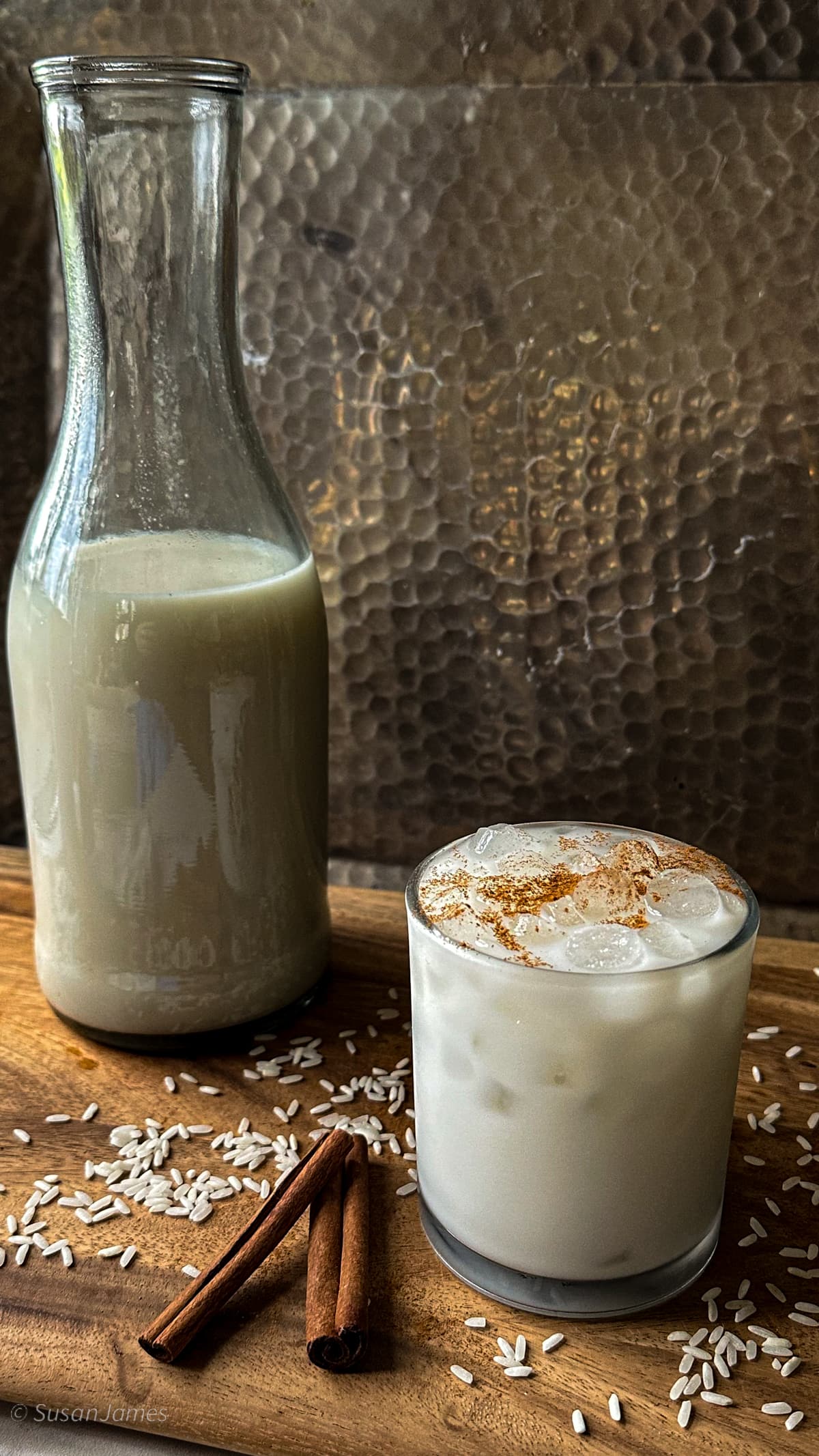 Horchata in a glass on a wood board with cinnamon sticks and rice.