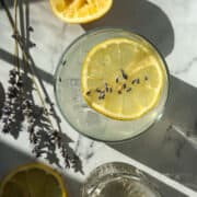 Lavender Lemonade in a glass next to lavender stems and lemon slices.