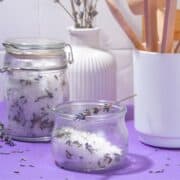 Lavender sugar in a glass jar on a purple table.