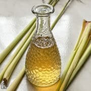 Lemongrass simple syrup in a small glass bottle on a white counter with lemongrass stalks on the side.